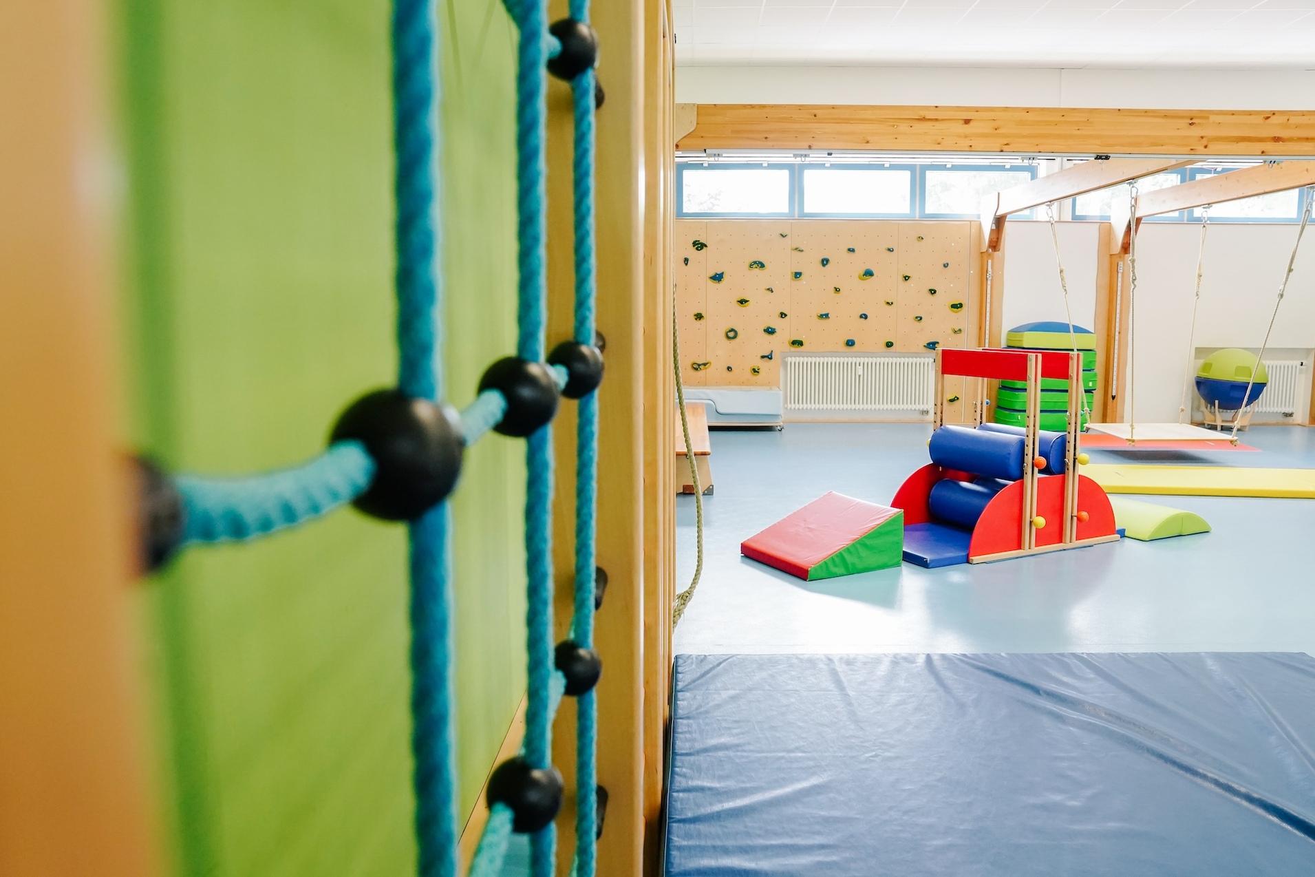 Spielraum mit Kletterwand, Turngeräten und Weichböden in freundlicher, gut beleuchteter Umgebung.