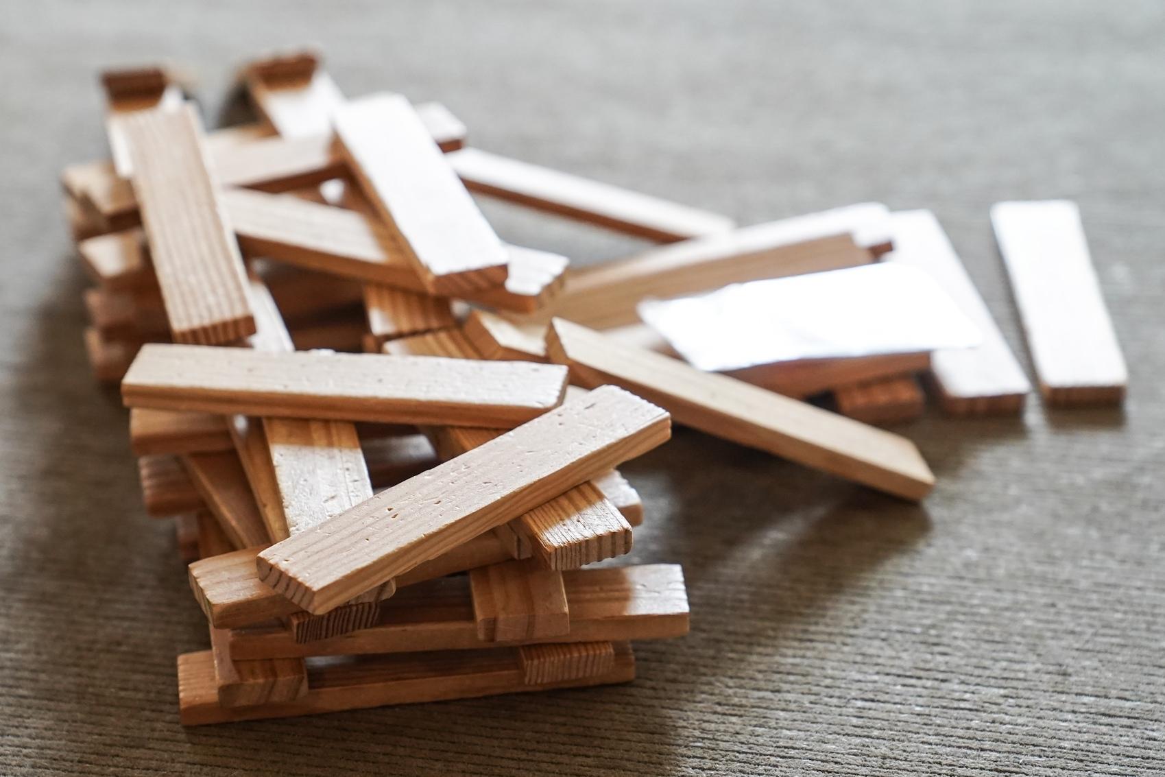 Ein Haufen aus Holzstäbchen liegt chaotisch auf einer grauen Oberfläche.